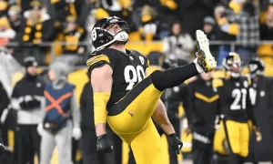 A football player in a black and yellow jersey celebrates energetically, raising one leg and expressing excitement in a packed stadium.