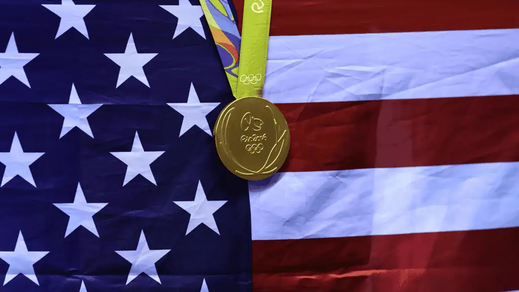 A gold Olympic medal hangs against the backdrop of the American flag, symbolizing victory and national pride.
