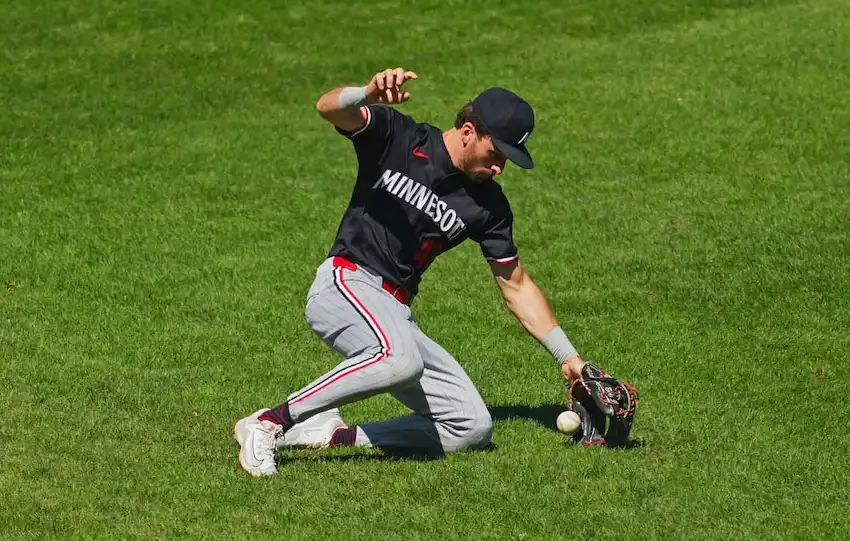 9 Minnesota baseball player attempts to field a ground ball while kneeling on the outfield grass.