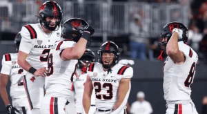 Ball State football players celebrate on the field wearing their black and white uniforms, showcasing team spirit and excitement.