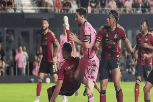 A tense soccer match moment with players in red and black jerseys challenging one another, showcasing dynamic athletic action on the field.