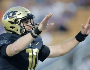 A UCF Knights football player in a black uniform and gold helmet signals to teammates during a game.