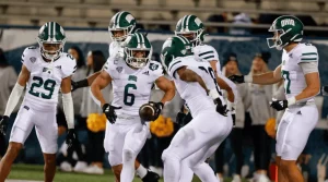 A football team in white uniforms celebrates a play on the field, with players showcasing teamwork and excitement during a game.
