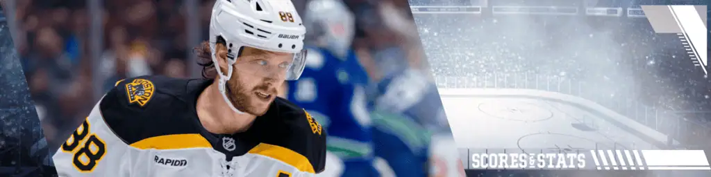 Washington Capitals vs Boston Bruins Picks and Predictions December 31st 2024 2 A hockey player in a black and yellow jersey skates on the ice, with a blurred crowd and scoreboard in the background.