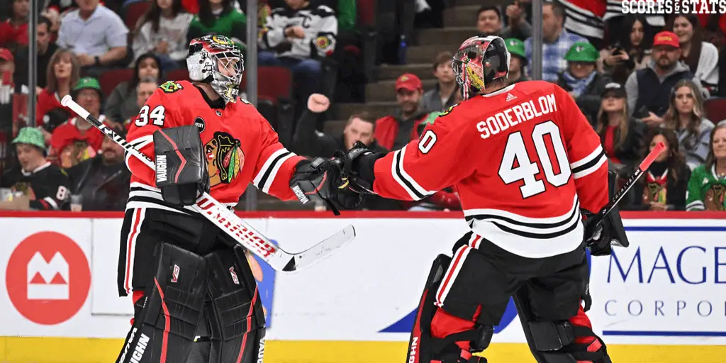 Chicago Blackhawks vs Dallas Stars Picks and Predictions December 29th 2024 2 Two hockey players in red jerseys celebrate on the ice, with a lively crowd in the background. One is dressed as a goalie.