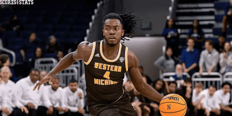 Michigan State Spartans vs Western Michigan Broncos Picks and Predictions December 30th 2024 3 Western Michigan basketball player dribbles the ball during a game, wearing a brown uniform with a crowd in the background.