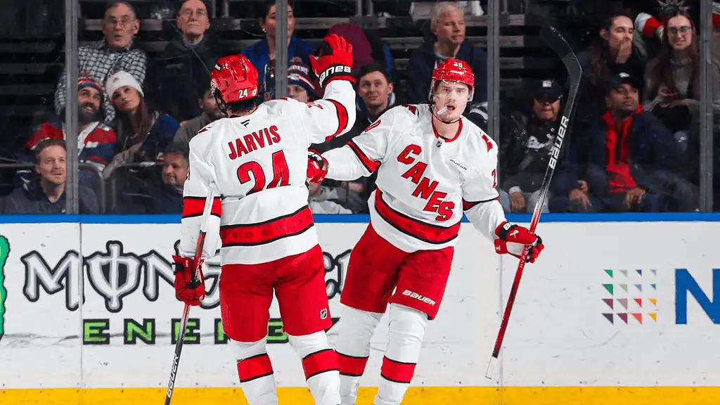 Columbus Blue Jackets vs Carolina Hurricanes Picks and Predictions December 31st 2024 2 Two hockey players in red and white jerseys celebrate a goal, with one raising their arm in triumph on the ice. Fans visible in the background.