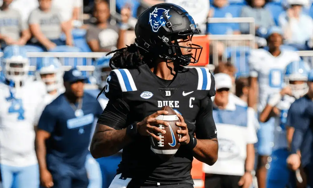 Ole Miss Rebels vs Duke Blue Devils Picks and Predictions January 2nd 2025 3 Duke football player in black jersey stands poised to pass with a football, surrounded by teammates and fans in the background.