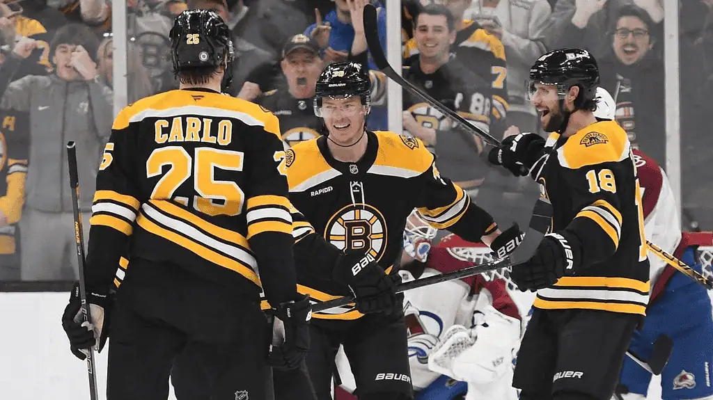 Buffalo Sabres vs Boston Bruins Picks and Predictions January 28th 2025 3 Three Boston Bruins players celebrate a goal during an ice hockey match, with fans cheering in the background.