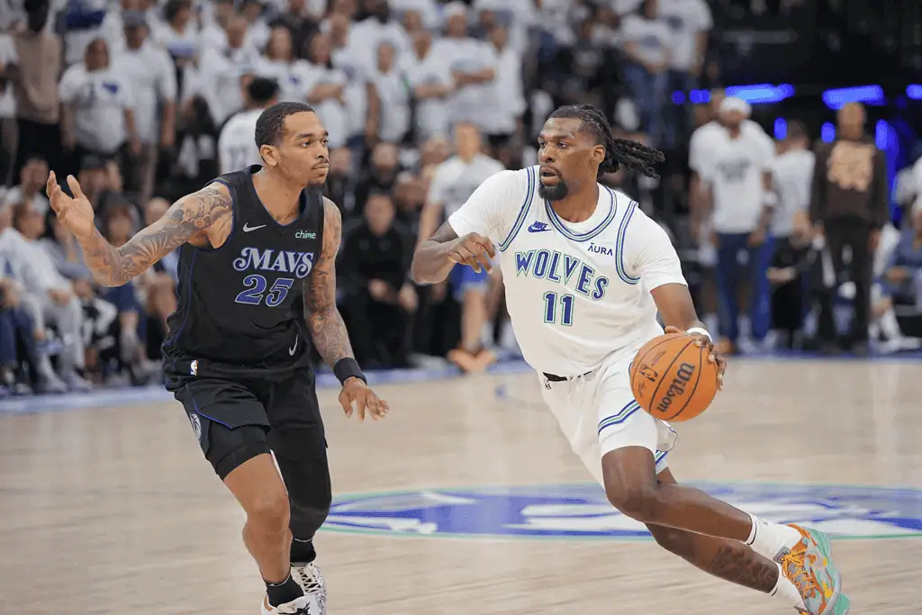 Memphis Grizzlies vs Minnesota Timberwolves Picks and Predictions January 20th 2025 2 A basketball player in a white jersey labeled "Wolves" dribbles while being guarded by an opponent in a black "Mavs" jersey on the court.