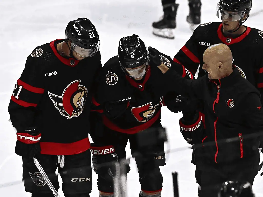 New York Islanders vs Ottawa Senators Picks and Predictions January 14th 2025 2 Ottawa Senators hockey players assist an injured teammate wearing number 2 off the ice, while a team trainer provides support during a game.