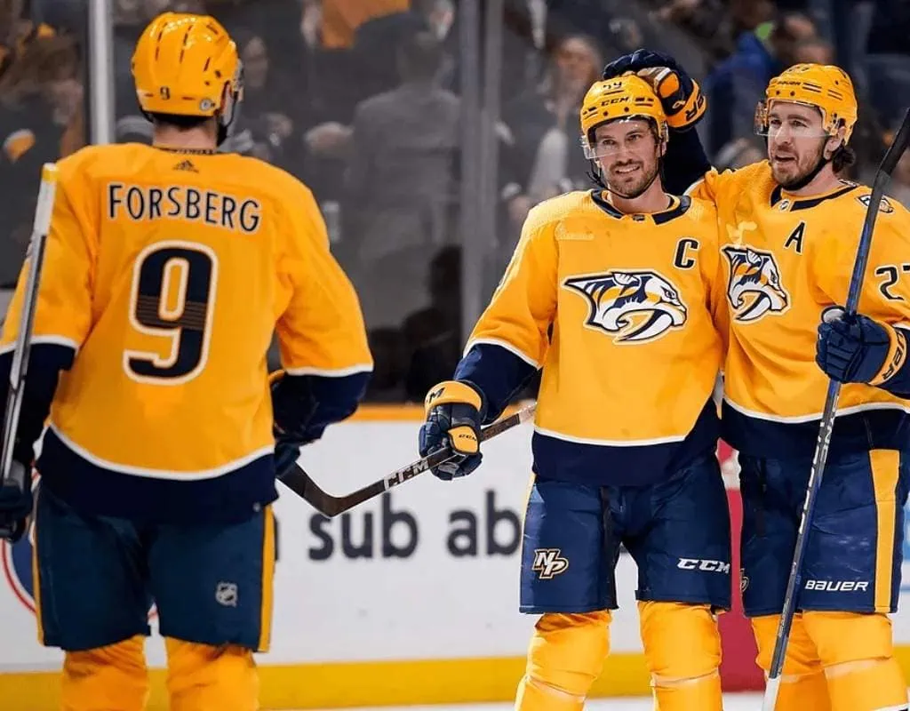 San Jose Sharks vs Nashville Predators Picks and Predictions January 23rd 2025 2 Three hockey players in bright yellow uniforms celebrate a goal on the ice, with one player smiling and raising a stick in triumph.