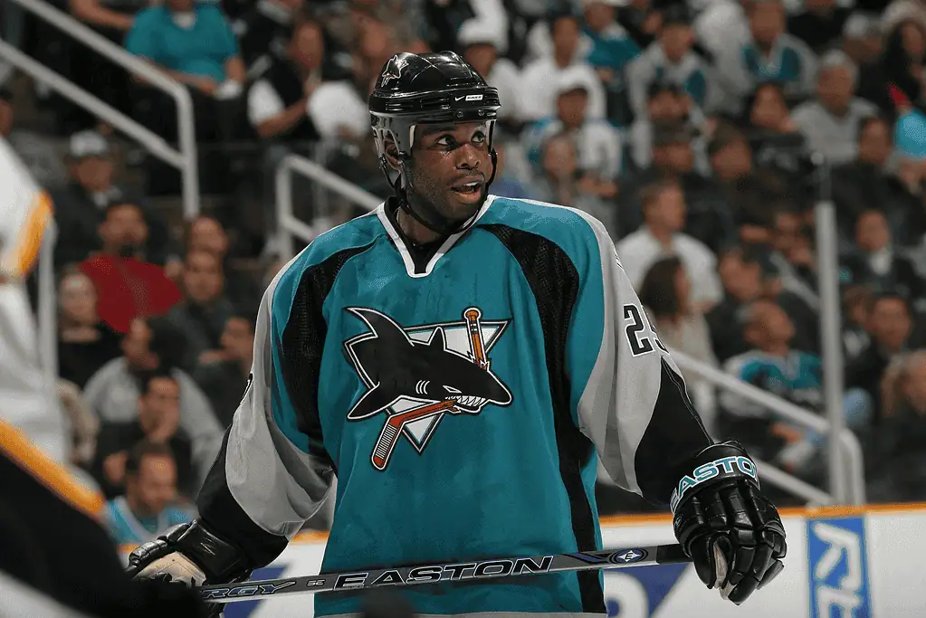 Detroit Red Wings vs San Jose Sharks Picks and Predictions January 14th 2025 2 A hockey player in a turquoise jersey featuring a shark logo stands on the rink, holding a hockey stick, with an engaged crowd in the background.