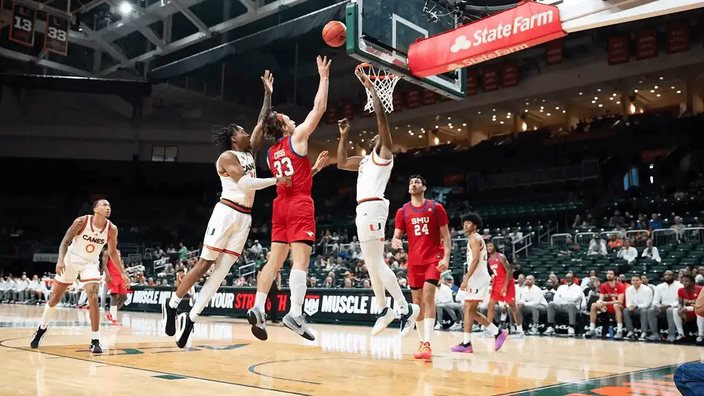 Smu Mustangs vs Louisville Cardinals Picks and Predictions January 21st 2025 2 A basketball player wearing red jumps to shoot a ball while two opposing players in white attempt to block the shot during a game.