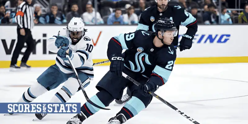 Columbus Blue Jackets vs Seattle Kraken Picks and Predictions January 9th 2025 2 Seattle Kraken player in a navy uniform with teal accents skating swiftly past a diving opponent in a white and teal jersey during an NHL game.