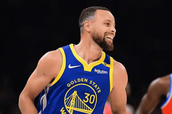 Golden State Warriors vs Utah Jazz Picks and Predictions January 28th 2025 3 Stephen Curry, wearing a blue Golden State Warriors jersey, smiles while playing on the court.