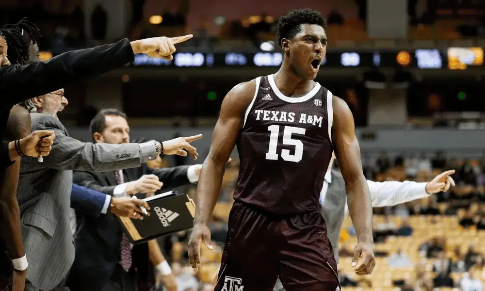 Texas A&m Aggies vs Oklahoma Sooners Picks and Predictions January 28th 2025 2 A Texas A&M basketball player in a maroon jersey stands confidently, receiving encouragement from team coaches and teammates during a game.