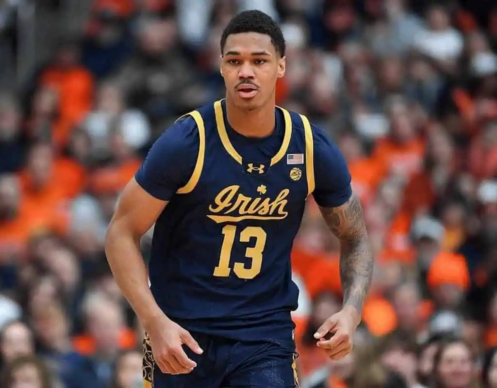 Duke Blue Devils vs Notre Dame Fighting Irish Picks and Predictions January 11th 2025 3 A basketball player in a navy blue jersey with "Irish" and number 13 runs energetically on the court amidst a cheering crowd.