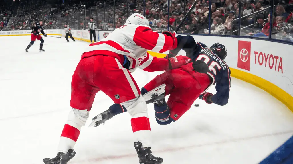 Detroit Red Wings vs Anaheim Ducks Picks and Predictions February 23rd 2025 2 A hockey player in a red uniform checks an opponent in blue, sending him crashing to the ice during an intense game.