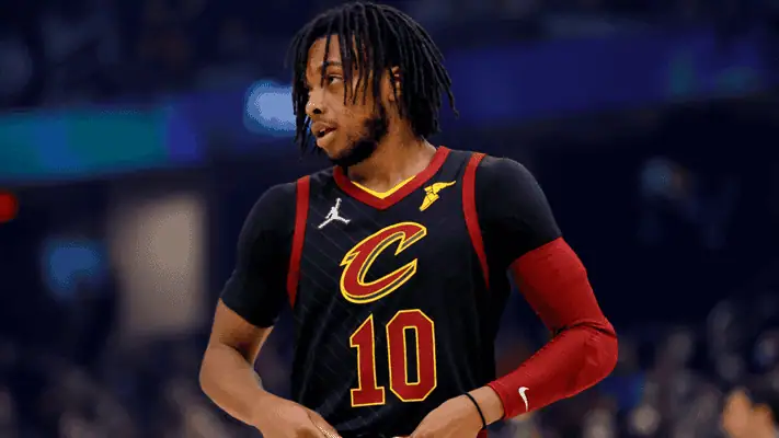  A Cleveland Cavaliers basketball player wearing a black jersey with red accents and number 10 looks to the side during a game, with the arena crowd blurred in the background.