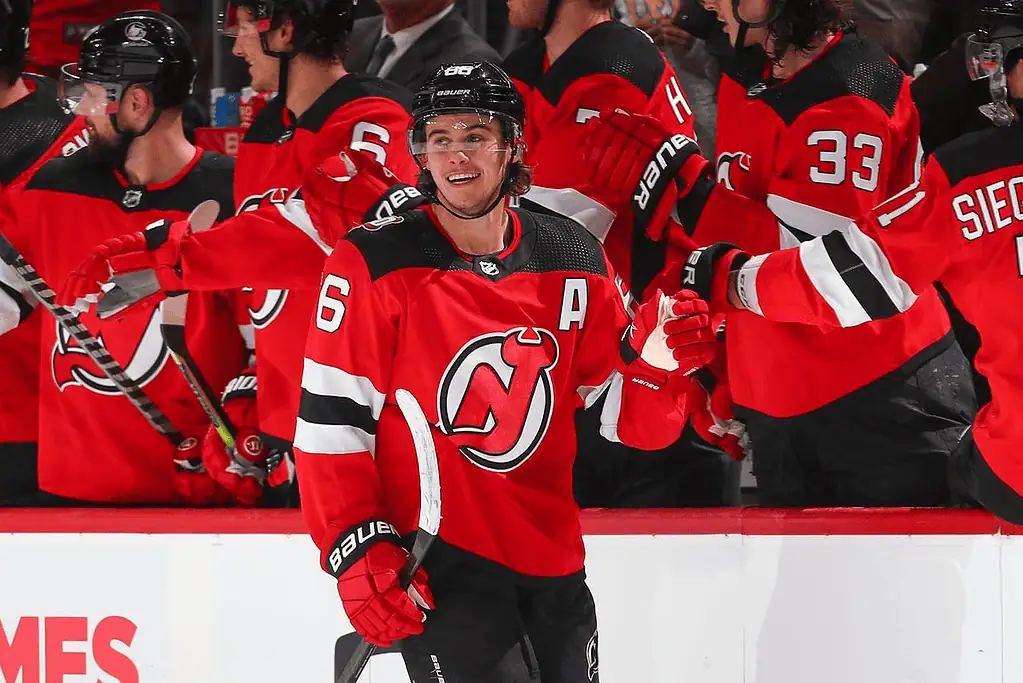 New Jersey Devils vs Vegas Golden Knights Picks and Predictions February 6th 2025 2 A hockey player in a red jersey with an "A" for captain celebrates with teammates on the bench, showcasing team spirit and excitement.