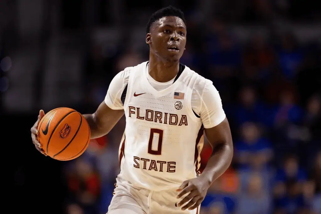 Florida State Seminoles vs North Carolina Tar Heels Picks and Predictions February 24th 2025 3 A basketball player in a white Florida State uniform dribbles a ball, focused on the game amidst a cheering crowd.