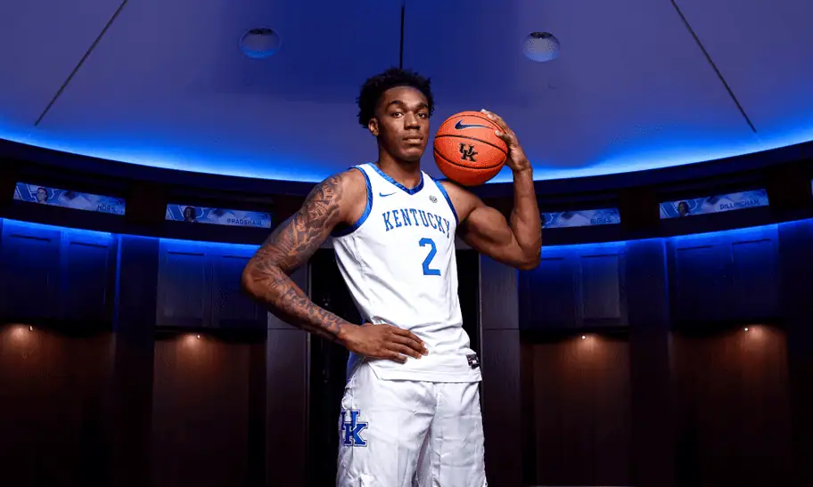 Alabama Crimson Tide vs Kentucky Wildcats Picks and Predictions February 22nd 2025 2 University of Kentucky basketball player posing with a basketball inside a blue-lit locker room.