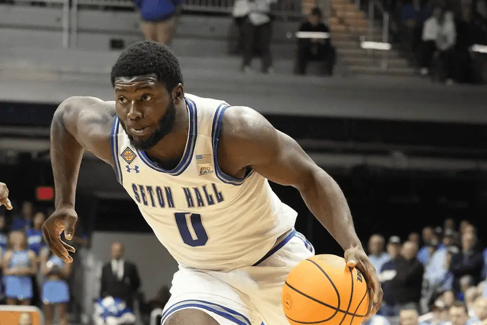 Depaul Blue Demons vs Seton Hall Pirates Picks and Predictions February 2nd 2025 2 A basketball player in a white and blue Seton Hall jersey dribbles a ball during an intense game, showcasing athleticism and focus.