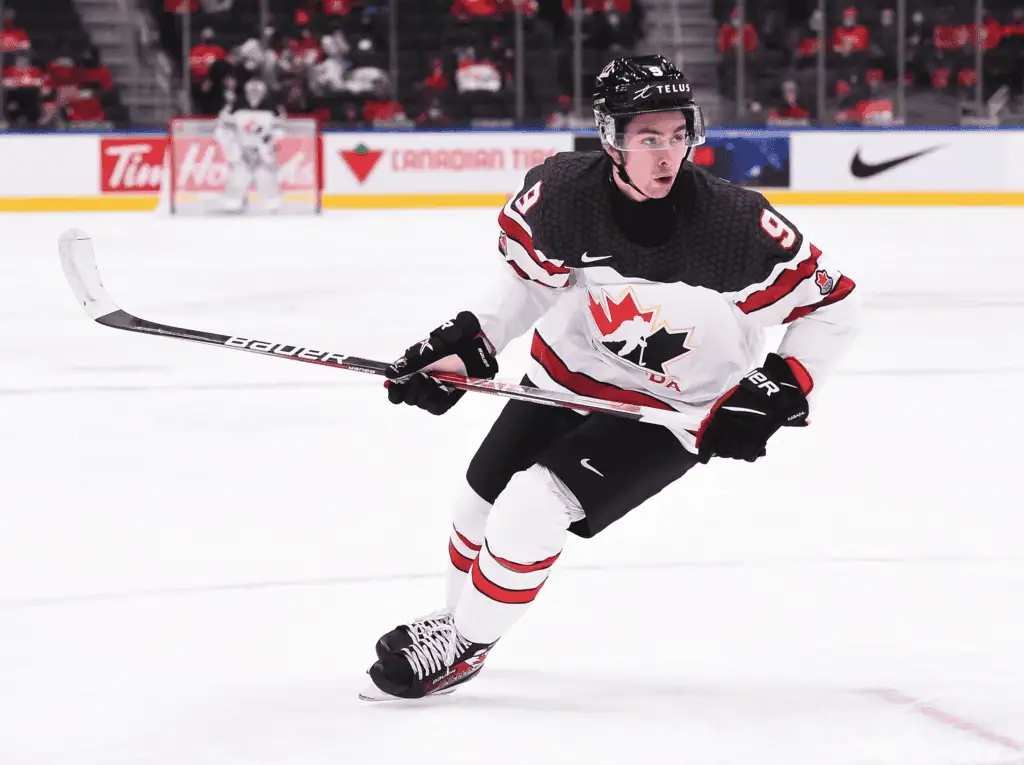 Team Canada ice hockey player wearing jersey number 9 skates across the rink while holding a Bauer hockey stick during an international match