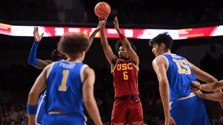 Usc Trojans vs Penn State Lady Lions Picks and Predictions February 11th 2025 2 USC basketball player wearing a red jersey taking a jump shot while surrounded by UCLA players in blue jerseys during a college basketball game.