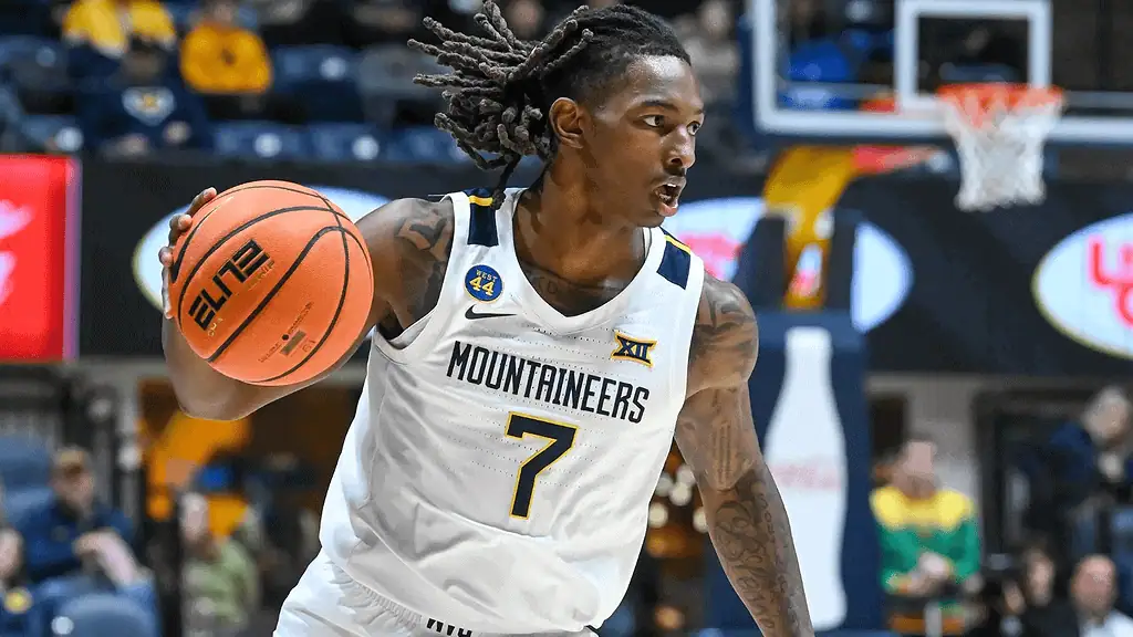Cincinnati Bearcats vs West Virginia Mountaineers Picks and Predictions February 2nd 2025 2 A basketball player in a white Mountaineers jersey dribbles a ball on the court, surrounded by spectators in a lively arena.