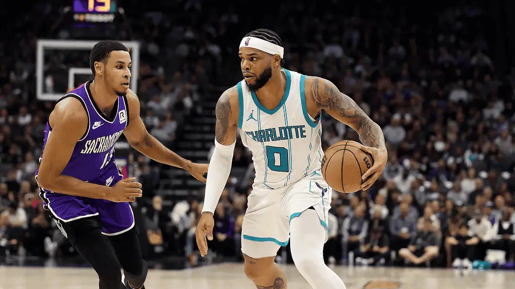 Charlotte Hornets vs Golden State Warriors Picks and Predictions March 3rd 2025 3 A basketball player in a white jersey with "Charlotte" insignia dribbles past a defender in a purple jersey during a game.