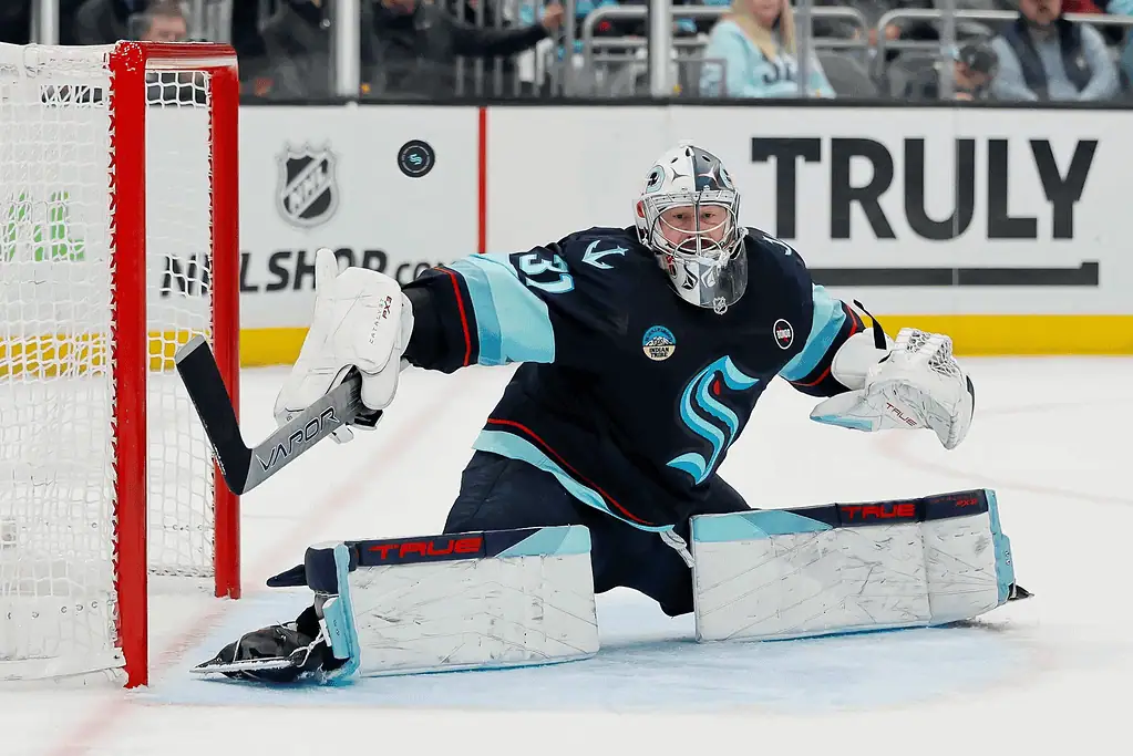A goalie in a navy uniform makes a save during an intense hockey match, with the puck flying toward the net.