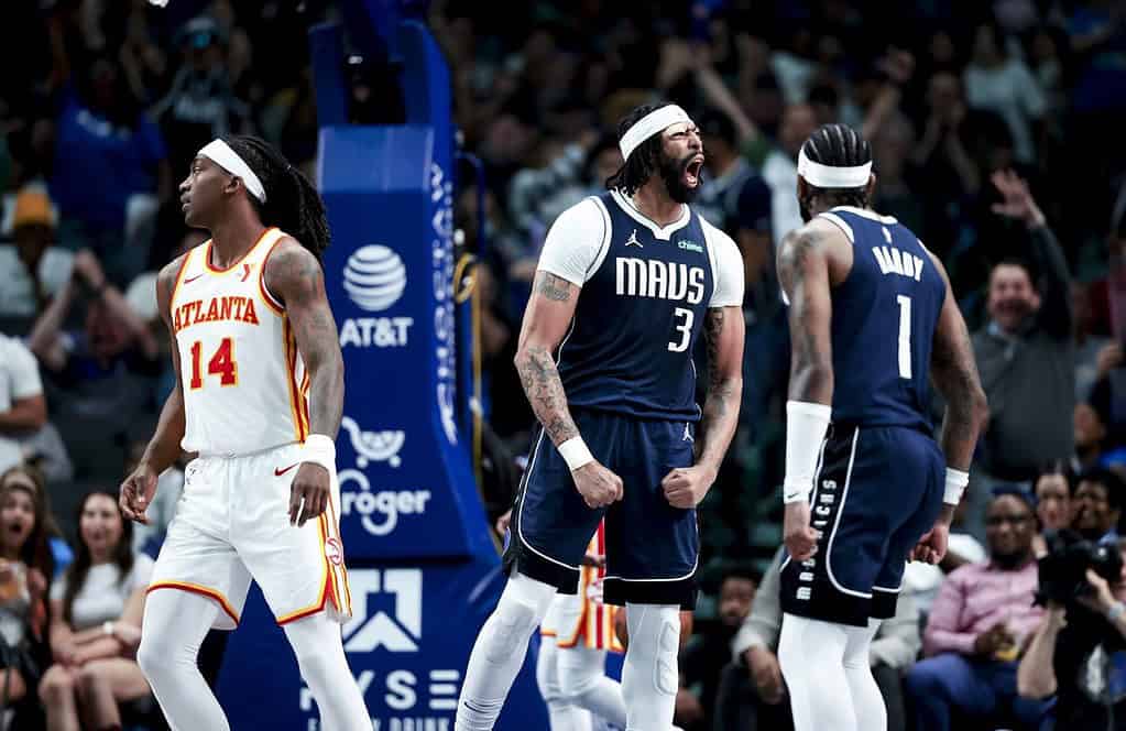 Two basketball players in dark uniforms celebrate on the court while another player in a light uniform looks on during a game.