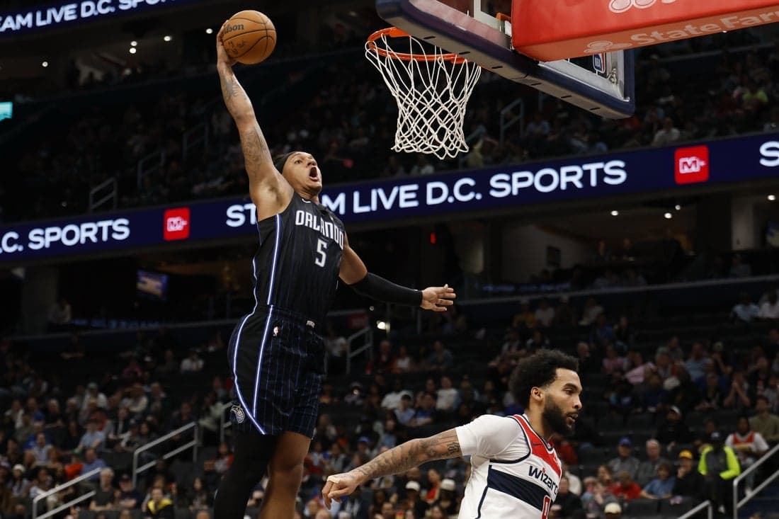3 A basketball player in a blue Orlando jersey leaps for a dunk, showcasing athleticism above an opponent in a white jersey.