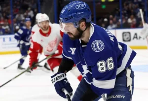 A hockey player in a blue uniform prepares to receive the puck during an intense game against a rival team in red uniforms.