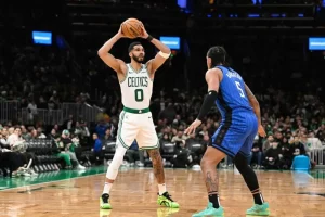 A player in a Celtics jersey prepares to shoot a basketball while being guarded by a player in a blue jersey during a game.