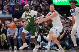 A basketball player in a green Milwaukee jersey dribbles while being closely guarded by an opponent in a white jersey during a game.