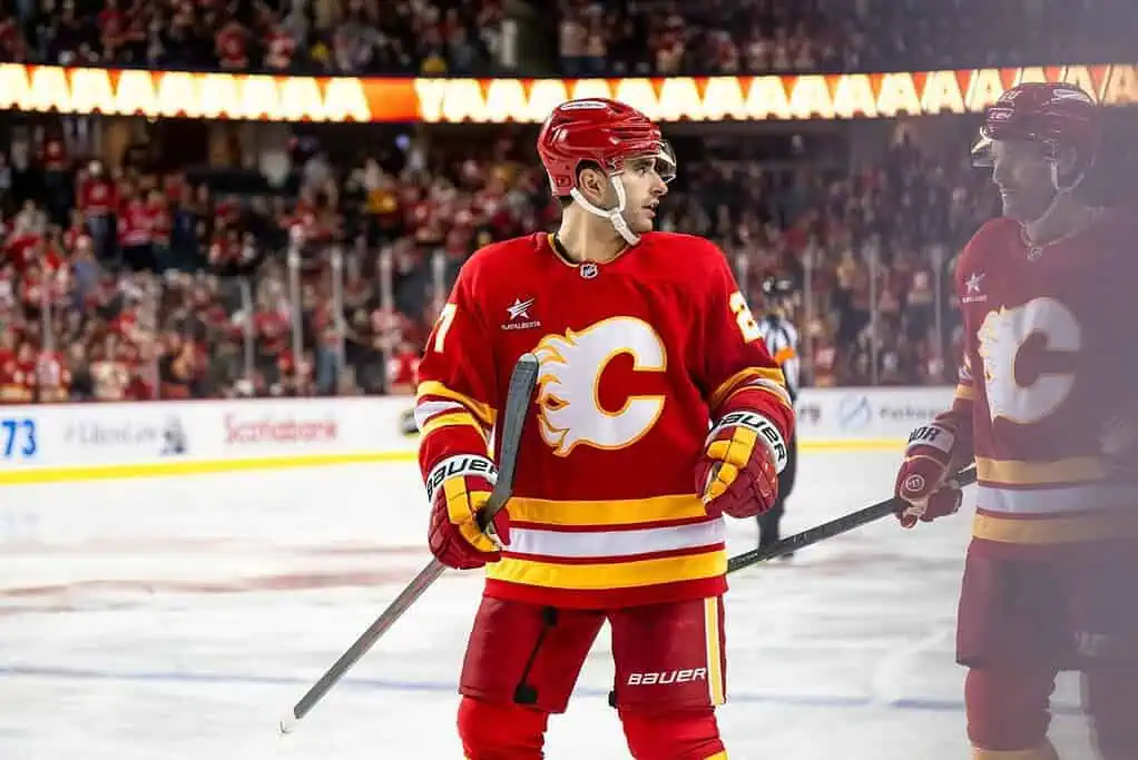 NHL 7 A Calgary Flames player in a red jersey stands on the ice, with fans cheering in the background during an intense hockey game.