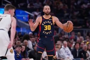 A basketball player in a Golden State jersey dribbles the ball, focused on the opposing player during a game.