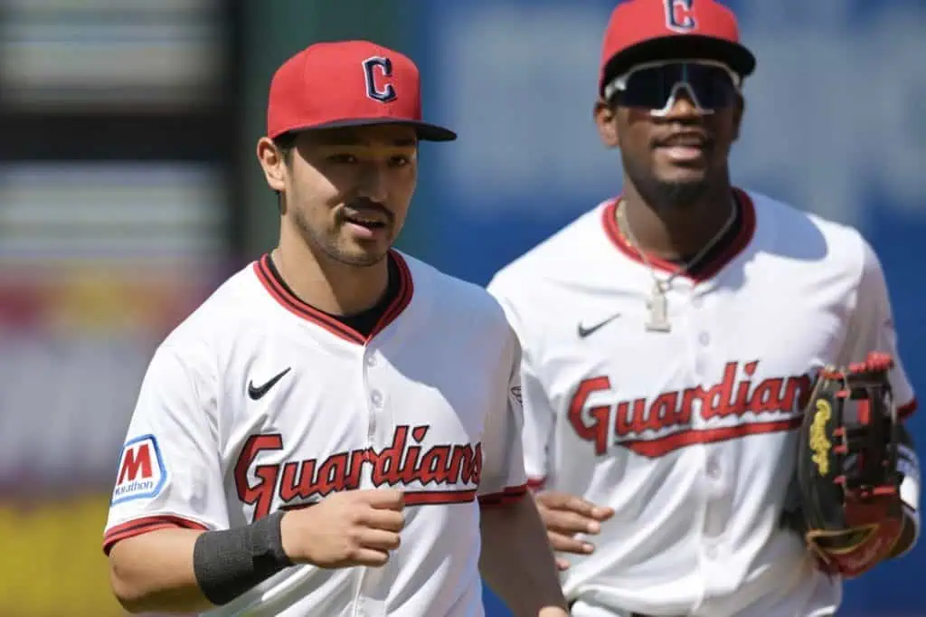 5 Two baseball players wearing white jerseys with "Guardians" on the front and red caps jogging together on the field.