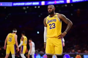 A player in a yellow Los Angeles Lakers jersey stands on the court during a game, with teammates visible in the background.