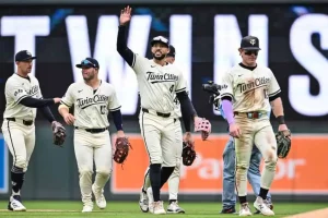 A group of baseball players in matching "Twin Cities" uniforms walk off the field, with one player waving to the crowd.