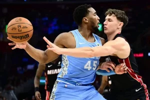 A basketball player in a blue jersey attempts a pass while being closely guarded by an opponent in a black jersey during a game.