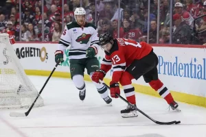 A hockey match in action, featuring players from the Minnesota Wild and New Jersey Devils competing for the puck amidst a cheering crowd.