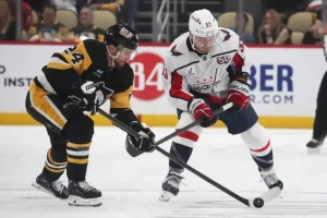 Two hockey players compete fiercely for the puck on an ice rink, showcased in their team's jerseys and protective gear.