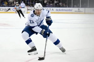 A Tampa Bay Lightning player glides over the ice, preparing to shoot the puck while wearing a white and blue uniform.