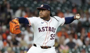 A pitcher in a white Astros uniform, poised to throw, holding a baseball with a vibrant orange glove.