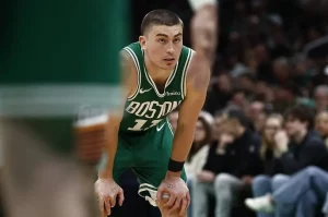 A basketball player in a green Boston Celtics uniform leans forward in exhaustion, with fans visible in the background.