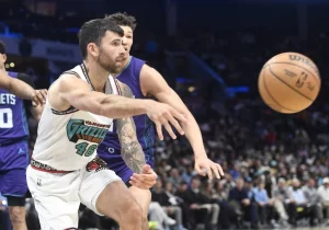 A basketball player in a Vancouver Grizzlies jersey passes the ball during an intense game, with spectators visible in the background.